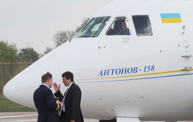 People talk as a Ukrainian Antonov-158 mid-range passenger plane stands on the tarmac of the Antonov plant airfield during a ceremony to commemorate its maiden flight in Kiev