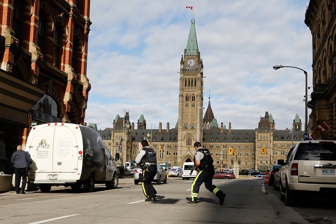Armed RCMP officers race across a street on Parliament Hilll following a shooting incident in Ottawa