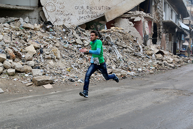 A participant runs past a damaged building as he competes in a running race along a street in Aleppo's Bustan al-Qasr neighborhood