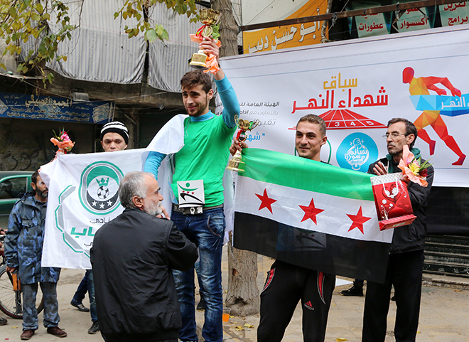 Ahmad Sobhe holds up a trophy as he celebrates winning a running race in Aleppo's Bustan al-Qasr neighbourhood